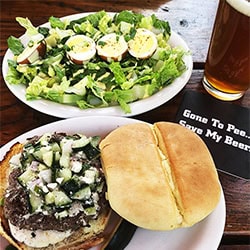 burger with fresh relish, salad with beer brined boiled eggs, and a beer with a coaster that says "gone to pee, watch my beer."